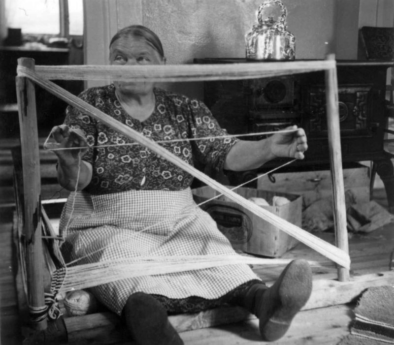 Kvinne som sitter på gulvet og bruker den tradisjonelle renningstolen og grindvev for å lage jarekanten til greneveven