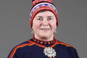 Nærbilde av kvinne med gobbagahpir. Hun har blått bomullstøy, rødt bånd og hvitt bånd nederst på luen. Luebåndet hennes er vevd.