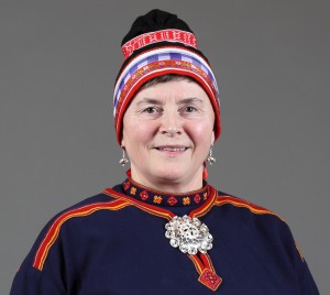 Nærbilde av kvinne med gobbagahpir. Hun har blått bomullstøy, rødt bånd og hvitt bånd nederst på luen. Luebåndet hennes er vevd.