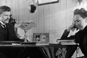 anders larsen s 13-14 Anders LArsen sitter vedet bord med en dame som leser.