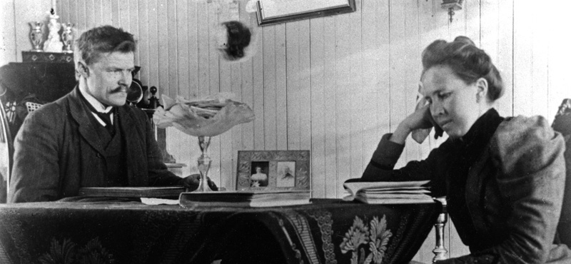 Anders LArsen sitter vedet bord med en dame som leser.