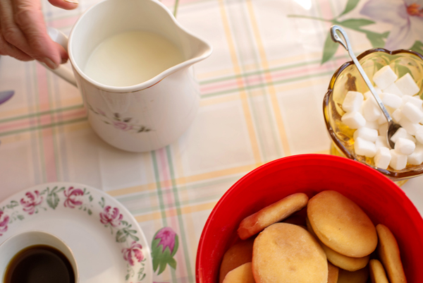 KJøkkenbord med kjeks, skål med sukkerbiter, kopp med kaffe, skål med melk.